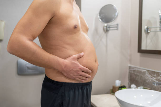 Overweight Problem Belly Man Looking At Himself İn The Mirror excess fat stock pictures, royalty-free photos & images