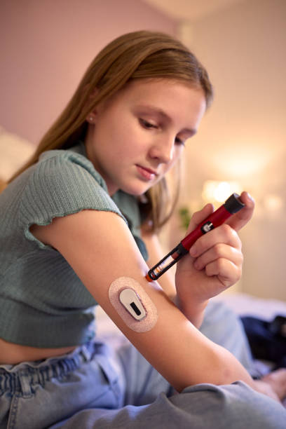 young diabetic girl sitting on bed in bedroom at home using kit to measure and check insulin levels - diabetes home interior blood sugar test healthcare and medicine imagens e fotografias de stock
