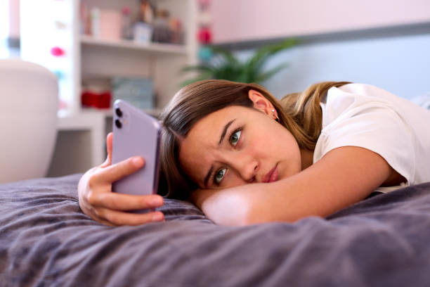 Adolescente deprimida deitada na cama em casa olhando para o telefone celular - foto de acervo