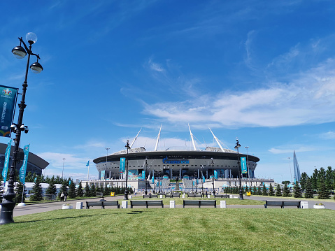 Saint-Petersburg. Russia. \nLawn and benches in front of the Gazprom Arena stadium in St. Petersburg on the morning of the match day of the EURO 2020 European Football Championship against a blue sky with clouds.