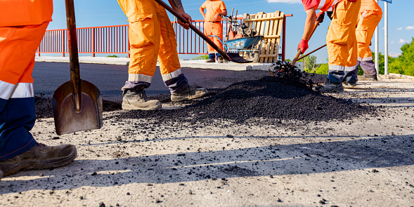 Zrenjanin, Vojvodina, Serbia - June 8, 2021: Few workers are using shovels to level, set up layer of fresh tarmac to right measures, pouring hot asphalt.