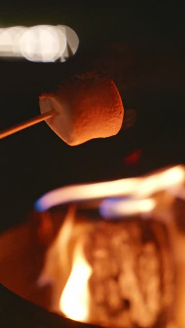 Closeup of a marshmallow being cooked on a campfire at night.