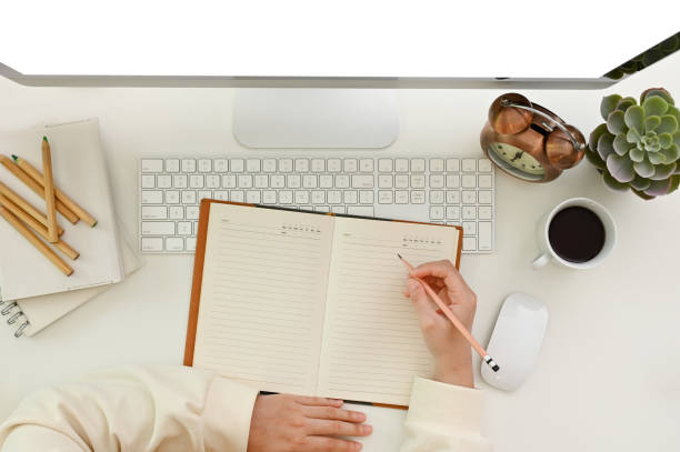 istock Top view of a modern workspace with a female's hand writing something on her notebook or diary 1465485133