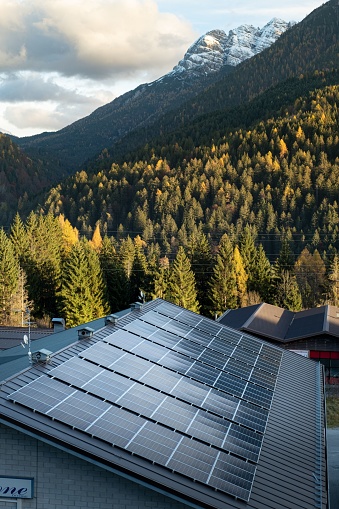 Shiny solar energy panels on house roofs near cascading green mountains in the daytime, vertical shot