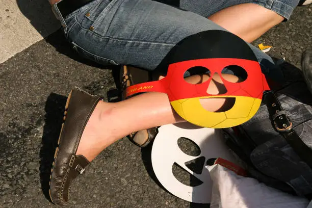 Public viewing: A face mask in black, red and gold lies on the knee of a participant who is sitting on the floor.