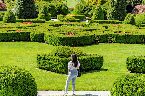 Young woman standingon path in beautiful green park with hedge shapes and trees at Arboretum volcji potok near Radomlje in Slovenia.