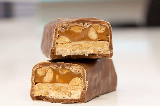 A closeup shot of a tasty caramel chocolate bar with peanuts on a white background