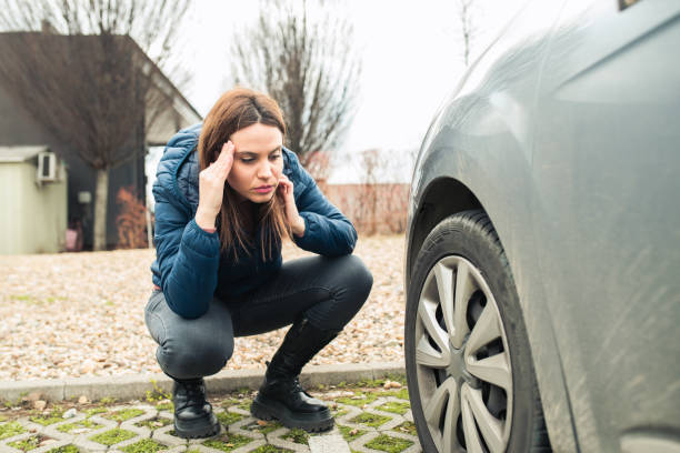 Young woman having a problem with her car tire Portrait of a despair young woman crouching next to her car with flat tire flat tire stock pictures, royalty-free photos & images