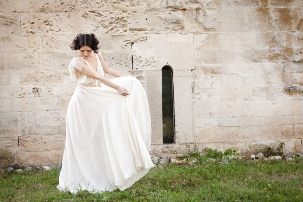 Elegant woman in white long dress looking down while holding the sides of her dress.