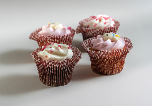 A closeup shot of four small cupcakes with cream and sprinkles on a white background