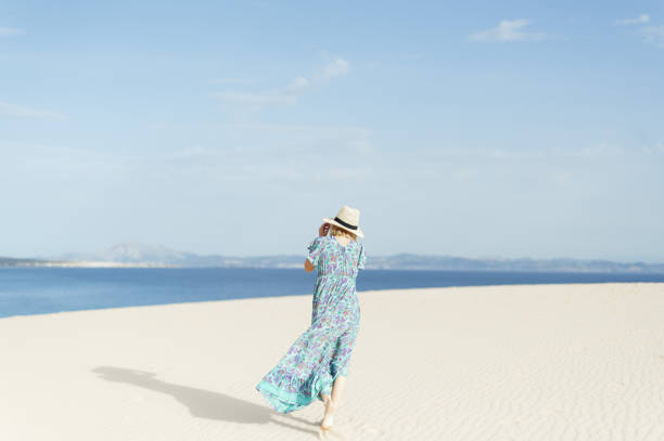 istock Young Spanish woman from behind walking on a white sandy beach with a hat 1465505452