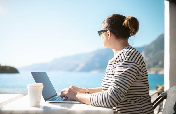 istock Working outdoors. Middle aged woman using laptop sitting on the beach and drinking coffee 1465505551
