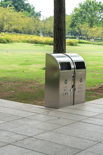 A vertical shot of trash cans in a modern park with a green and clean environment