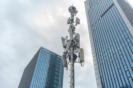 A closeup shot of a 5g transmission tower with modern buildings and sky for a copy space