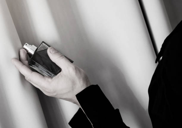 A hand sprays a perfume bottle onto a testing card, trying the fragrance in closeup. The scene shows a focused moment of scent testing and evaluation in a professional or personal setting.