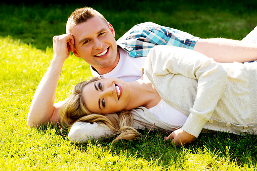 A young romantic couple lying on green grass and smiling