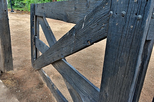 An old weathered, wooden, corral gate hangs partially opened.