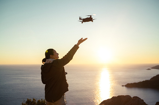 Woman operating drone and catching it in the air at sunset