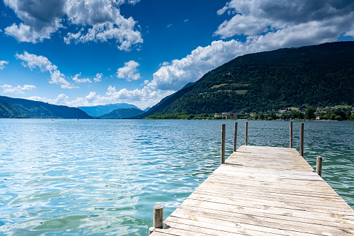 The photo shows a mountain panorama of Lake Annecy in France. The photo was taken outdoors on a sunny summer's day with blue sky and copy space. A paraglider is seen in the sky.