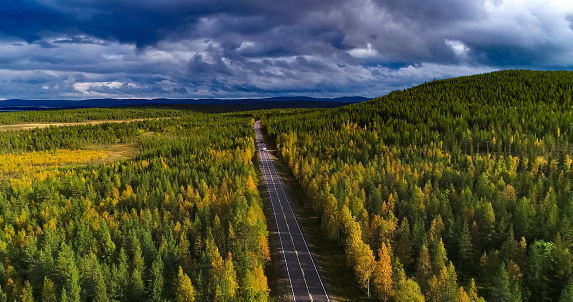 Aerial view following a white RV car driving on a fall road, between colorful autumn forest, sarkijarvi lake and fjeld mountains, Lapland, Finland
