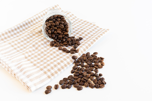 The roasted coffee beans thrown on white surface from the glass