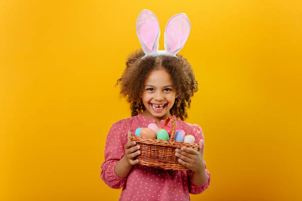 istock A girl is holding a basket full of Easter colored eggs on a yellow background 1465518745