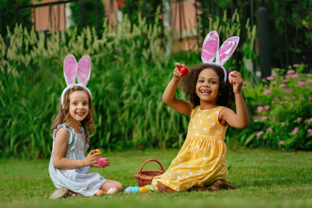 zwei mädchen bei der ostereiersuche und beim einlegen von ostereiern in körbe - easter easter egg child chocolate stock-fotos und bilder