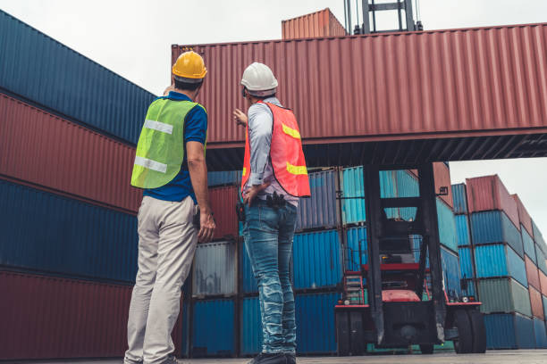 istock Industrial worker works with co-worker at overseas shipping container yard . Logistics supply chain management and international goods export concept . 1465520374