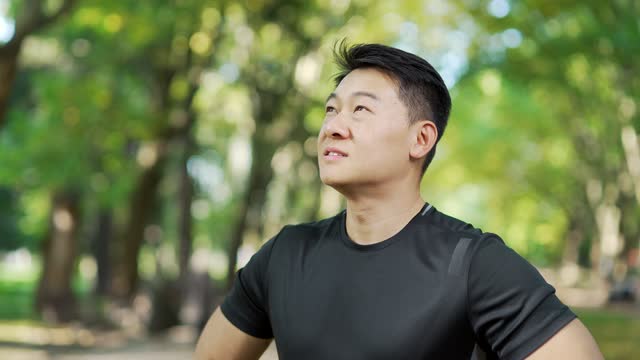 Close up of a young adult asian sports man relaxing with his eyes closed after a morning run while standing in an urban city park