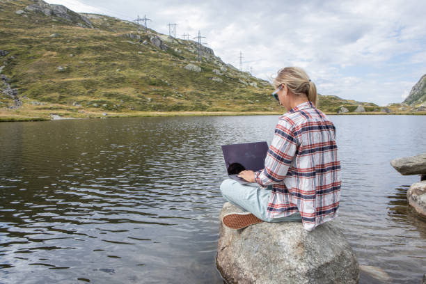 istock Woman sits on rock using laptop by the lake, remote working 1465523842