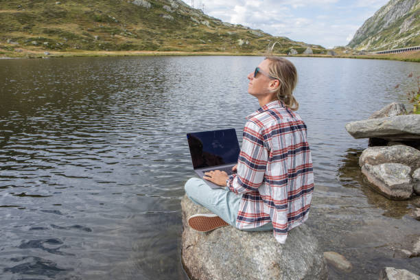 istock Woman sitting on a rock on lake shore uses laptop computer 1465524010