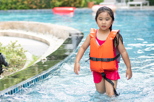 Asian girl wearing life jacket playing in swimming pool on summer