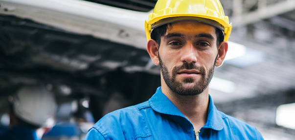 Portrait of handsome Caucasian young automotive mechanic or technician man looking at camera at garage at auto repair shop, after service concept