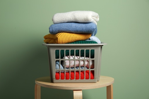 Plastic laundry basket with clean clothes on wooden table near light green wall