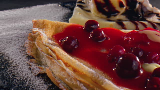 Sweet pancakes topped with cherry syrup, cheese, banana and chocolate