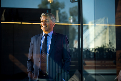 Happy businessman standing at office seen through glass window