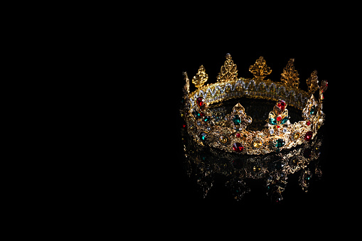 Beautiful golden crown with gems on dark mirror surface. Space for text