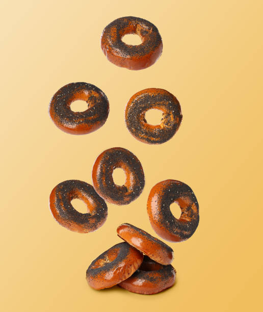 istock Many fresh bagels with poppy seeds falling into pile on light orange background 1465534513