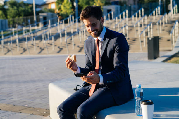 istock Businessman eating sandwich on lunch break outdoors. Man using phone and smiling 1465534531