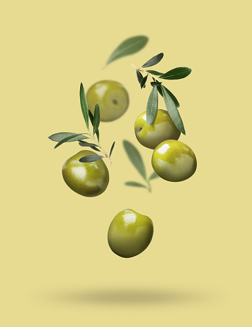 Fresh olives and leaves falling on pale yellow background