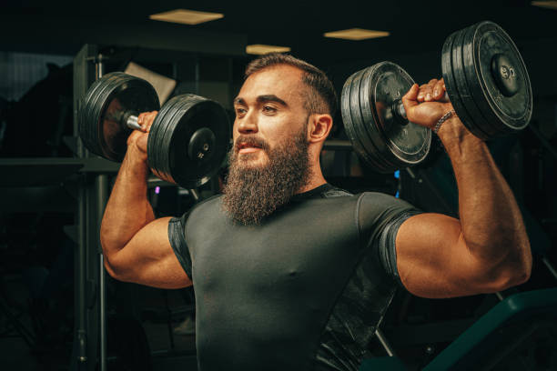 Muscular young man lifting weights in a dark gym stock photo