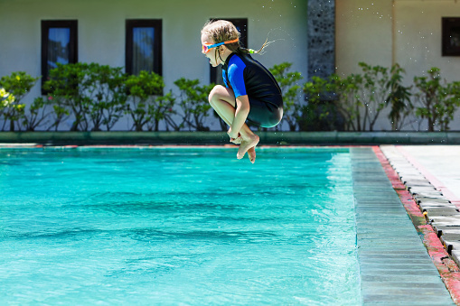 Happy child in wetsuit and goggles has fun jumping into swimming pool. Healthy family lifestyle, little kids water sports activity, swimming lessons with parents at training class