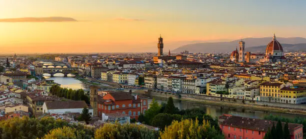 Photo of The Florence cityscape with the Ponte Vecchio over Arno river, the Palazzo Vecchio and the Florence Cathedral in an orange sunset.