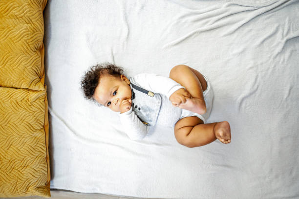 cute little baby boy lying down on a stretched out blanket after having his diaper changed, while sucking his right hand thumb and holding his left feet in other hand - thumb sucking cute small lying down imagens e fotografias de stock