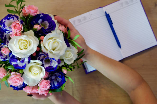 istock Flatlay. Female hands hold a bouquet of multi-colored roses flower. Notebook, diary with a pen on a wooden table 1465540975