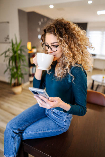 istock Young woman relaxing at home, drinking coffee and using mobile phone 1465543315