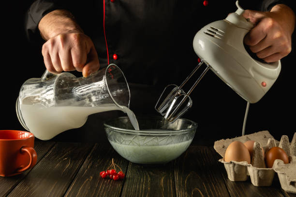 istock Professional chef prepares a delicious breakfast with milk and eggs in the kitchen using an electric hand mixer. The cook pours the poloko into a deep plate. Delicious recipe menu for hotel. 1465543740