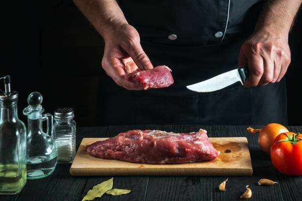 istock Chef cutting beef meat with knife on kitchen, cooking food. Vegetables and spices on kitchen table to prepare delicious lunch 1465544272