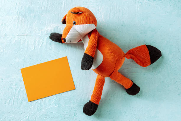 Mockup with an orange greeting card and a toy fox. A mock-up