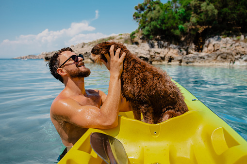 Handsome bearded men having fun with his dog on vacation. They are using kayak. Surrounded by sea rocks and woods.